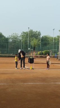 Delhi, Hindistan, 17 Şubat 2025 - Maha Open için kil tenis kortunda antrenörlük yapan genç tenisçiler, yaklaşan turnuva için küçük tenis oyuncuları antrenman yapıyor