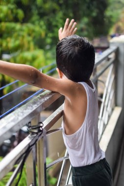 Yaz yağmurunda oynayan küçük çocuk evin balkonunda, Hintli akıllı çocuk yağmur mevsiminde yağmur damlalarıyla oynuyor, çocuk yağmurda oynuyor.