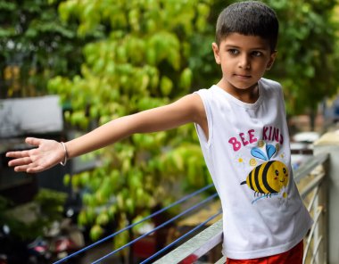 Yaz yağmurunda oynayan küçük çocuk evin balkonunda, Hintli akıllı çocuk yağmur mevsiminde yağmur damlalarıyla oynuyor, çocuk yağmurda oynuyor.