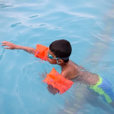 Havuzda yüzen mutlu Hintli çocuk, sıcak yaz tatillerinde hava tüpüyle birlikte yüzen çocuk, büyük bir havuzda yüzen çocuk..