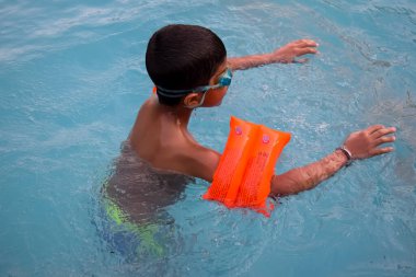 Havuzda yüzen mutlu Hintli çocuk, sıcak yaz tatillerinde hava tüpüyle birlikte yüzen çocuk, büyük bir havuzda yüzen çocuk..