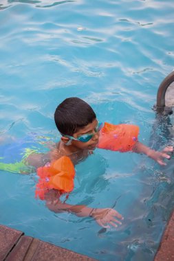 Havuzda yüzen mutlu Hintli çocuk, sıcak yaz tatillerinde hava tüpüyle birlikte yüzen çocuk, büyük bir havuzda yüzen çocuk..