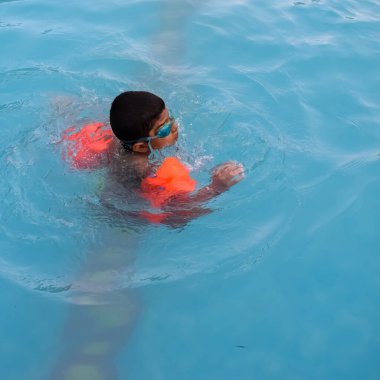 Havuzda yüzen mutlu Hintli çocuk, sıcak yaz tatillerinde hava tüpüyle birlikte yüzen çocuk, büyük bir havuzda yüzen çocuk..
