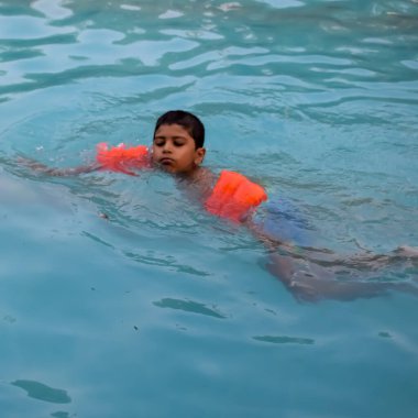 Havuzda yüzen mutlu Hintli çocuk, sıcak yaz tatillerinde hava tüpüyle birlikte yüzen çocuk, büyük bir havuzda yüzen çocuk..