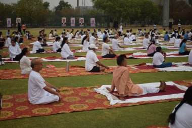 Yeni Delhi, Hindistan, 21 Haziran 2025 - Uluslararası Yoga Günü 'nde Delhi' deki Yamuna Spor Kompleksi 'nde grup Yoga egzersiz oturumu, kriket stadyumunda yoga sınıfına katılan büyük bir grup yetişkin