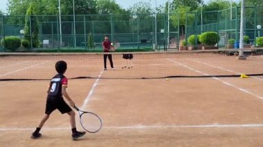 Delhi, Hindistan, 17 Şubat 2025 - Maha Open için kil tenis kortunda antrenörlük yapan genç tenisçiler, yaklaşan turnuva için küçük tenis oyuncuları antrenman yapıyor