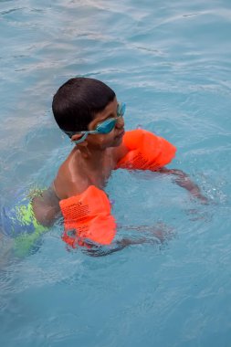 Havuzda yüzen mutlu Hintli çocuk, sıcak yaz tatillerinde hava tüpüyle birlikte yüzen çocuk, büyük bir havuzda yüzen çocuk..