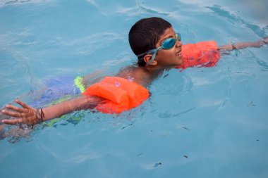 Havuzda yüzen mutlu Hintli çocuk, sıcak yaz tatillerinde hava tüpüyle birlikte yüzen çocuk, büyük bir havuzda yüzen çocuk..