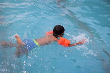 Havuzda yüzen mutlu Hintli çocuk, sıcak yaz tatillerinde hava tüpüyle birlikte yüzen çocuk, büyük bir havuzda yüzen çocuk..