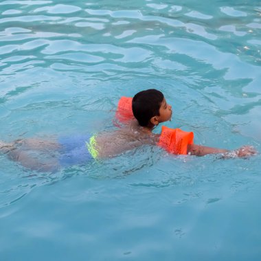 Havuzda yüzen mutlu Hintli çocuk, sıcak yaz tatillerinde hava tüpüyle birlikte yüzen çocuk, büyük bir havuzda yüzen çocuk..