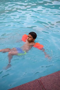 Havuzda yüzen mutlu Hintli çocuk, sıcak yaz tatillerinde hava tüpüyle birlikte yüzen çocuk, büyük bir havuzda yüzen çocuk..
