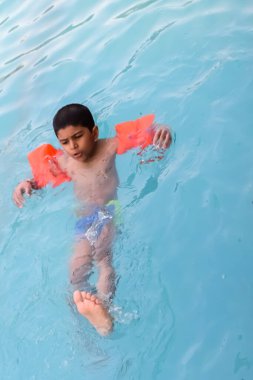 Havuzda yüzen mutlu Hintli çocuk, sıcak yaz tatillerinde hava tüpüyle birlikte yüzen çocuk, büyük bir havuzda yüzen çocuk..