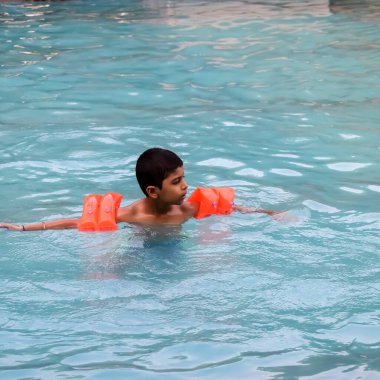 Havuzda yüzen mutlu Hintli çocuk, sıcak yaz tatillerinde hava tüpüyle birlikte yüzen çocuk, büyük bir havuzda yüzen çocuk..