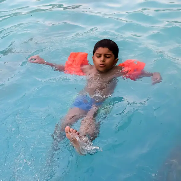 Havuzda yüzen mutlu Hintli çocuk, sıcak yaz tatillerinde hava tüpüyle birlikte yüzen çocuk, büyük bir havuzda yüzen çocuk..