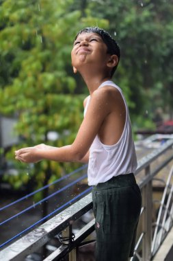 Yaz yağmurunda oynayan küçük çocuk evin balkonunda, Hintli akıllı çocuk yağmur mevsiminde yağmur damlalarıyla oynuyor, çocuk yağmurda oynuyor.