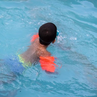 Havuzda yüzen mutlu Hintli çocuk, sıcak yaz tatillerinde hava tüpüyle birlikte yüzen çocuk, büyük bir havuzda yüzen çocuk..