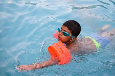 Havuzda yüzen mutlu Hintli çocuk, sıcak yaz tatillerinde hava tüpüyle birlikte yüzen çocuk, büyük bir havuzda yüzen çocuk..