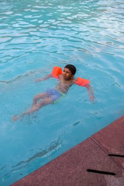 Havuzda yüzen mutlu Hintli çocuk, sıcak yaz tatillerinde hava tüpüyle birlikte yüzen çocuk, büyük bir havuzda yüzen çocuk..