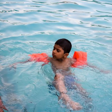 Havuzda yüzen mutlu Hintli çocuk, sıcak yaz tatillerinde hava tüpüyle birlikte yüzen çocuk, büyük bir havuzda yüzen çocuk..