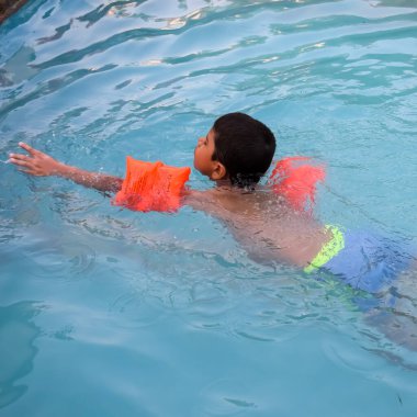 Havuzda yüzen mutlu Hintli çocuk, sıcak yaz tatillerinde hava tüpüyle birlikte yüzen çocuk, büyük bir havuzda yüzen çocuk..