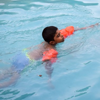 Havuzda yüzen mutlu Hintli çocuk, sıcak yaz tatillerinde hava tüpüyle birlikte yüzen çocuk, büyük bir havuzda yüzen çocuk..