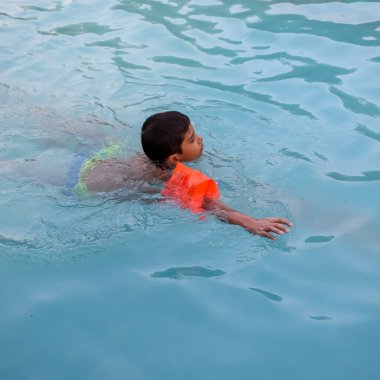 Havuzda yüzen mutlu Hintli çocuk, sıcak yaz tatillerinde hava tüpüyle birlikte yüzen çocuk, büyük bir havuzda yüzen çocuk..