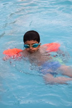 Havuzda yüzen mutlu Hintli çocuk, sıcak yaz tatillerinde hava tüpüyle birlikte yüzen çocuk, büyük bir havuzda yüzen çocuk..
