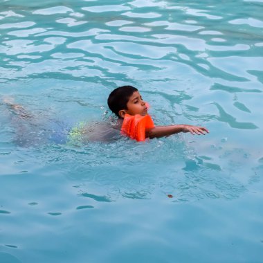 Havuzda yüzen mutlu Hintli çocuk, sıcak yaz tatillerinde hava tüpüyle birlikte yüzen çocuk, büyük bir havuzda yüzen çocuk..