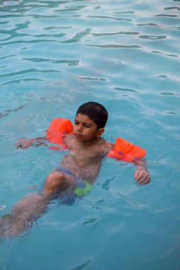 Havuzda yüzen mutlu Hintli çocuk, sıcak yaz tatillerinde hava tüpüyle birlikte yüzen çocuk, büyük bir havuzda yüzen çocuk..