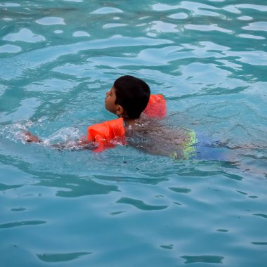 Havuzda yüzen mutlu Hintli çocuk, sıcak yaz tatillerinde hava tüpüyle birlikte yüzen çocuk, büyük bir havuzda yüzen çocuk..