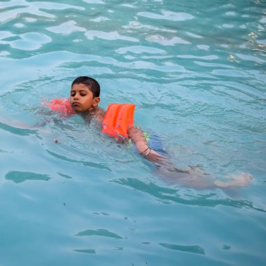 Havuzda yüzen mutlu Hintli çocuk, sıcak yaz tatillerinde hava tüpüyle birlikte yüzen çocuk, büyük bir havuzda yüzen çocuk..