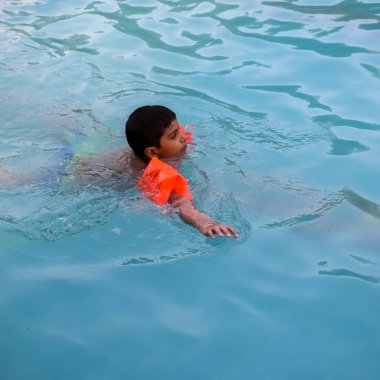 Havuzda yüzen mutlu Hintli çocuk, sıcak yaz tatillerinde hava tüpüyle birlikte yüzen çocuk, büyük bir havuzda yüzen çocuk..