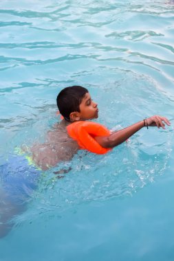 Havuzda yüzen mutlu Hintli çocuk, sıcak yaz tatillerinde hava tüpüyle birlikte yüzen çocuk, büyük bir havuzda yüzen çocuk..