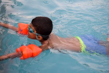 Havuzda yüzen mutlu Hintli çocuk, sıcak yaz tatillerinde hava tüpüyle birlikte yüzen çocuk, büyük bir havuzda yüzen çocuk..