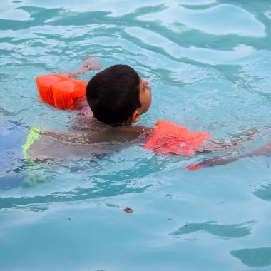 Havuzda yüzen mutlu Hintli çocuk, sıcak yaz tatillerinde hava tüpüyle birlikte yüzen çocuk, büyük bir havuzda yüzen çocuk..