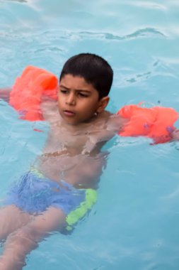 Havuzda yüzen mutlu Hintli çocuk, sıcak yaz tatillerinde hava tüpüyle birlikte yüzen çocuk, büyük bir havuzda yüzen çocuk..