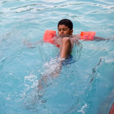 Havuzda yüzen mutlu Hintli çocuk, sıcak yaz tatillerinde hava tüpüyle birlikte yüzen çocuk, büyük bir havuzda yüzen çocuk..