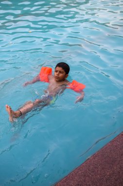 Havuzda yüzen mutlu Hintli çocuk, sıcak yaz tatillerinde hava tüpüyle birlikte yüzen çocuk, büyük bir havuzda yüzen çocuk..