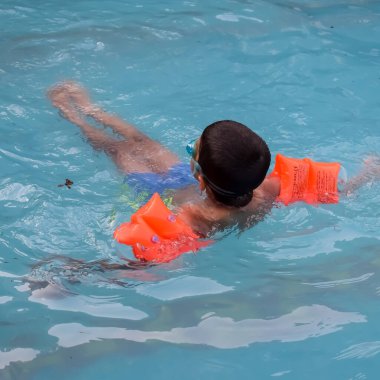 Havuzda yüzen mutlu Hintli çocuk, sıcak yaz tatillerinde hava tüpüyle birlikte yüzen çocuk, büyük bir havuzda yüzen çocuk..