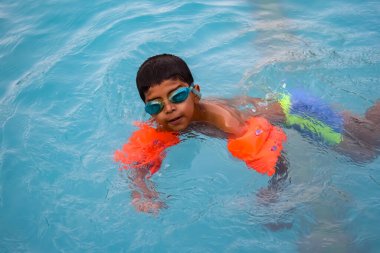 Havuzda yüzen mutlu Hintli çocuk, sıcak yaz tatillerinde hava tüpüyle birlikte yüzen çocuk, büyük bir havuzda yüzen çocuk..