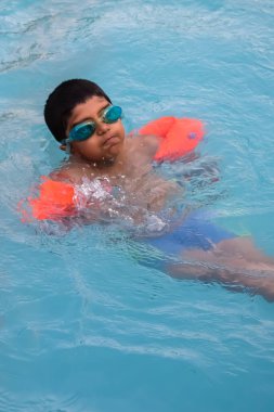 Havuzda yüzen mutlu Hintli çocuk, sıcak yaz tatillerinde hava tüpüyle birlikte yüzen çocuk, büyük bir havuzda yüzen çocuk..