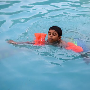 Havuzda yüzen mutlu Hintli çocuk, sıcak yaz tatillerinde hava tüpüyle birlikte yüzen çocuk, büyük bir havuzda yüzen çocuk..