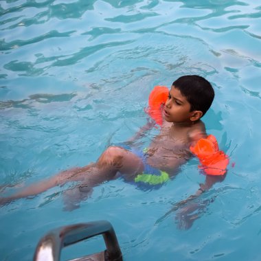 Havuzda yüzen mutlu Hintli çocuk, sıcak yaz tatillerinde hava tüpüyle birlikte yüzen çocuk, büyük bir havuzda yüzen çocuk..