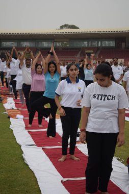 Yeni Delhi, Hindistan, 21 Haziran 2025 - Uluslararası Yoga Günü 'nde Delhi' deki Yamuna Spor Kompleksi 'nde grup Yoga egzersiz oturumu, kriket stadyumunda yoga sınıfına katılan büyük bir grup yetişkin