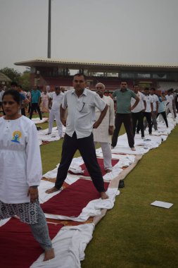 Yeni Delhi, Hindistan, 21 Haziran 2025 - Uluslararası Yoga Günü 'nde Delhi' deki Yamuna Spor Kompleksi 'nde grup Yoga egzersiz oturumu, kriket stadyumunda yoga sınıfına katılan büyük bir grup yetişkin