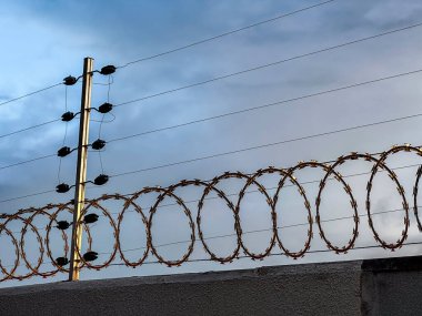 Arka planda dramatik bir gökyüzü olan bir duvarda elektrikli güvenlik çiti.