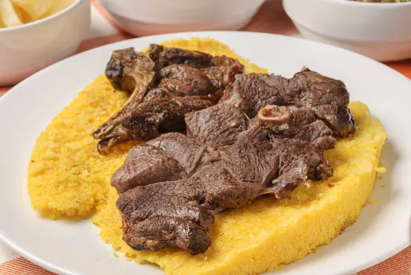 stock image Barbecue meat with Brazilian couscous, paired with rice, beans, cassava and vinaigrette, on a white plate on top of a white and orange checkered tablecloth. Northeastern Brazilian cuisine.