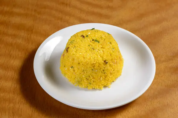 stock image Couscous from the northeast region of Brazil on a white plate on a wooden table.