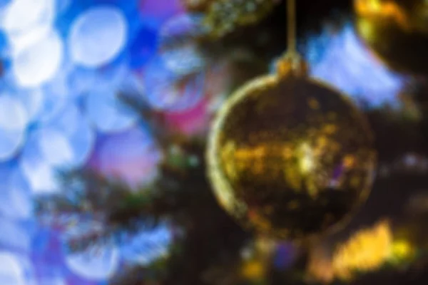 Closeup of Festively Decorated Outdoor Christmas tree with bright gold ball on blurred sparkling fairy background. Defocused garland lights, Bokeh effect. Christmas and New Year concept