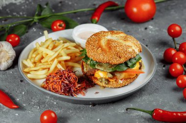 Peynirli hindi burger, marul, domates ve taze salatalık. Gri bir zemin üzerinde hindili pirzola ve patates kızartması sosu ve salata..